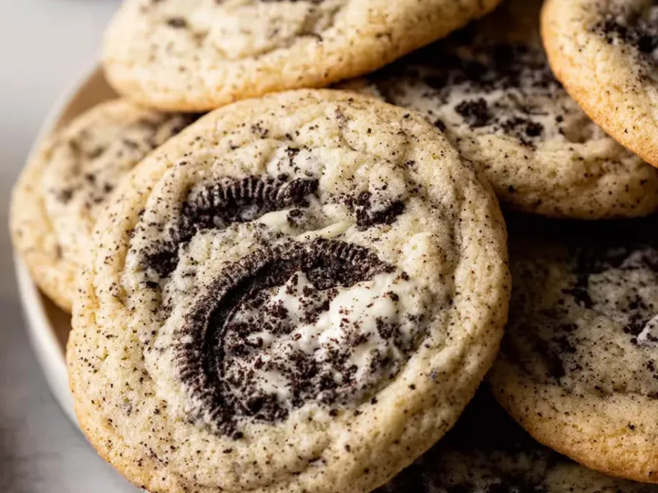 Large pale vanilla cookies studded with crushed chocolate sandwich cookie pieces, one with a cookie half pressed into the top