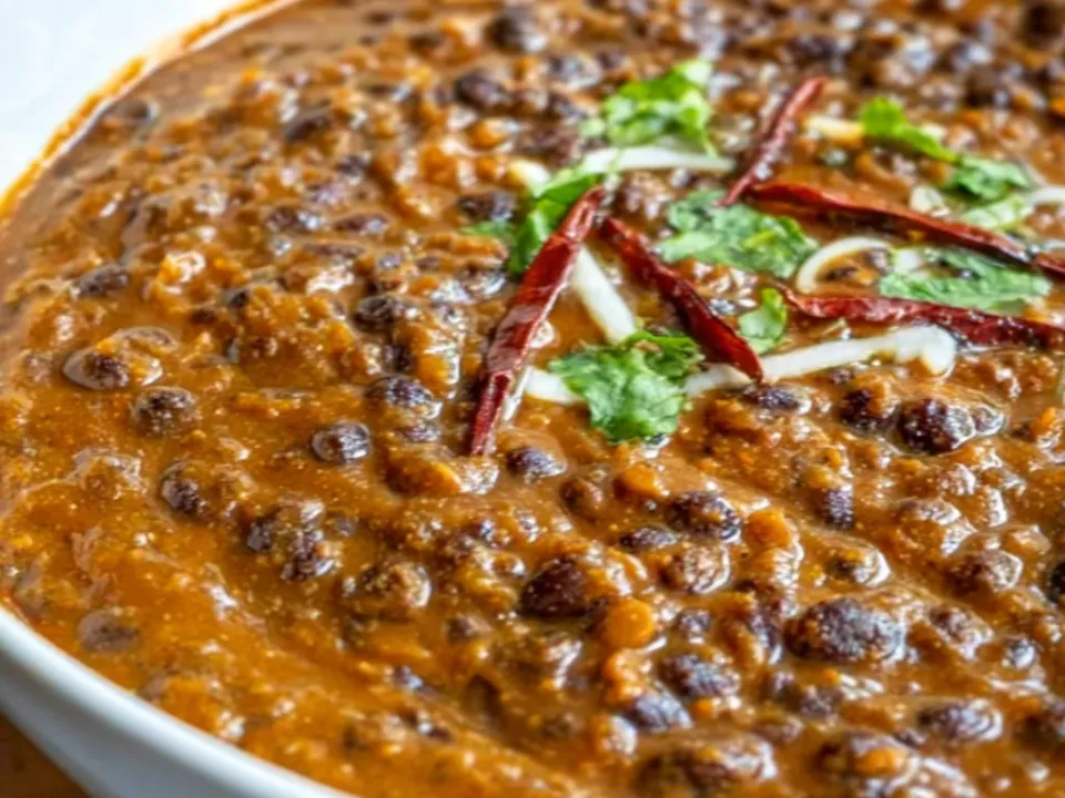 A bowl of thick dark brown creamy lentil curry with whole black lentils, a cream swirl, cilantro and dried red chillies on top
