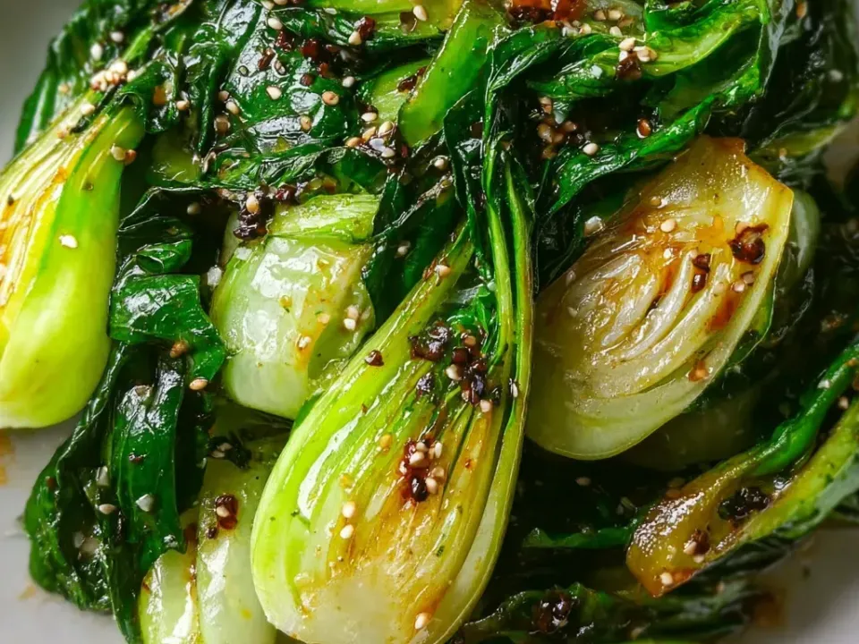 Halved baby bok choy sauteed until the leaves are dark green and the stems lightly browned, glossy with sauce and scattered with sesame seeds and pepper flakes